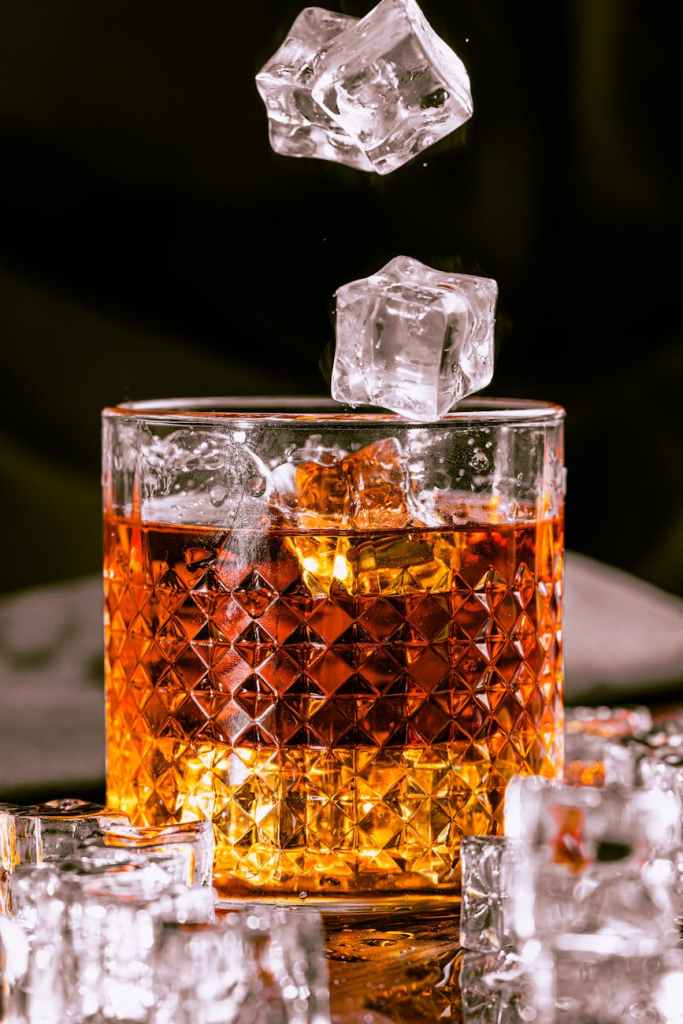 a glass of whiskey with ice cubes falling from it